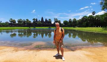 Person posing in front of Angkor Wat with reflective water in front.
