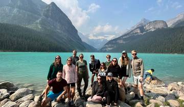Group of people posing in front of a turquoise lake and mountains.