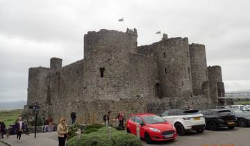 A castle with Welsh flags, people and cars in front.