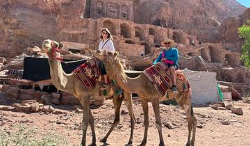 People riding camels in front of ancient rock-cut architecture.