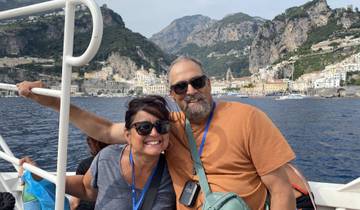 A couple smiling on a boat with the Amalfi Coast in the background.