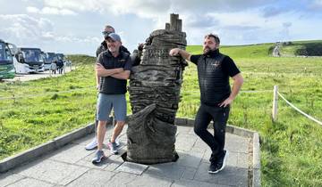 Men posing by a wooden sculpture with scenic cliffs in the background.