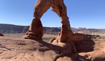 A person standing under a large natural rock arch in a desert landscape.