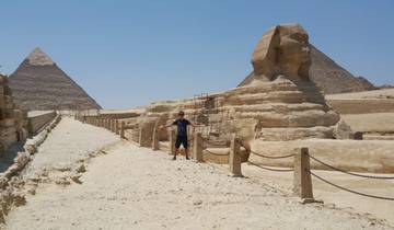 Person posing with arms stretched out in front of the Sphinx and Pyramid of Giza.