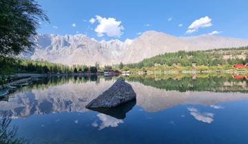 Mountain landscape reflected in a lake, with a prominent rock in the foreground.