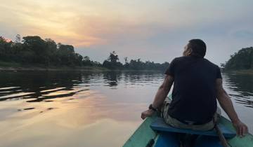 A person sitting on a boat looking at a sunset over a river with trees on the shore.