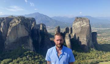Man standing in front of towering rocky formations with scenic mountains.