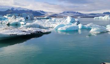 Serene lagoon with floating icebergs and mountains in the background.