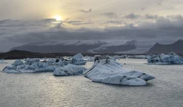 Icebergs floating in a lagoon under a cloudy sky.