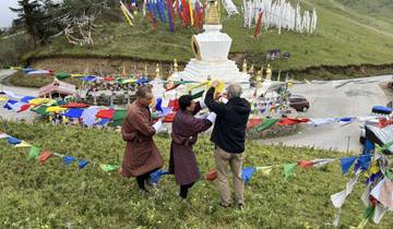 Three men hanging prayer flags near a white stupa.