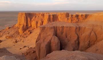 Orange cliffs in a desert landscape at sunset.