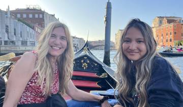 Two women on a boat in Venice with buildings lining the canal.