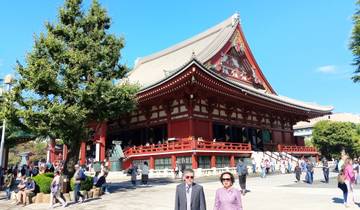 Traditional red temple building in Tokyo with visitors walking around.