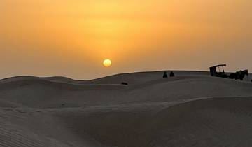 Desert landscape at sunset with people and a camel silhouette.
