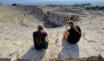 Two people sitting on ancient amphitheater steps admiring the view.