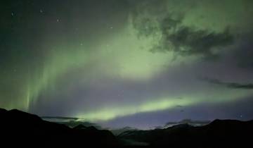 Northern lights in the night sky over mountains.