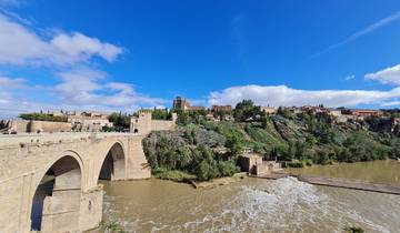 River with arched stone bridge and historic town on a hill.