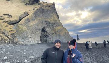 People standing on a black sand beach with basalt columns and a rocky cliff.