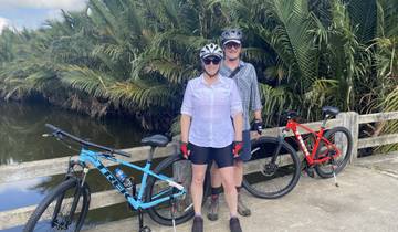 Two people standing with bicycles on a bridge surrounded by lush greenery.