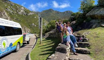 Group of people sitting on a stone ledge with mountains and a van nearby.