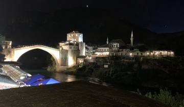 Mostar Bridge lit up at night over a river.