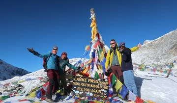 People posing by a Larke Pass sign surrounded by snowy mountains.