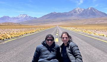 Two people sitting on a road with mountains in the background.