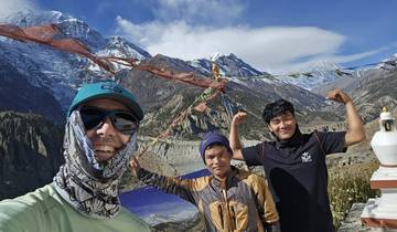 A group of hikers posing in front of mountainous scenery with prayer flags.