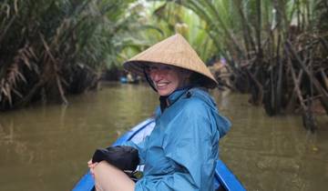 Woman enjoying a boat ride with conical hat in a waterway.