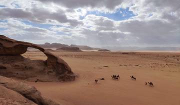Desert landscape with a natural arch and a caravan of camels.