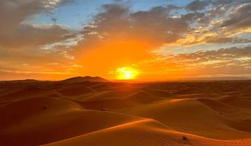 Sunset over sand dunes with a dramatic sky.