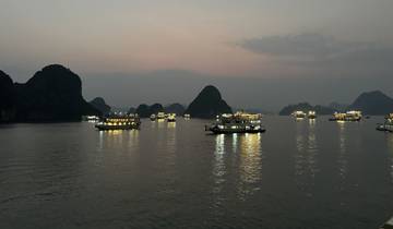 Boats with lights on a tranquil bay during twilight, likely in Halong Bay, Vietnam.