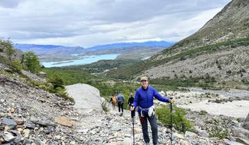 People hiking on a rocky path with a vast landscape and a lake in the distance.