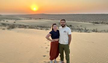 A couple standing on sand dunes at sunset, likely in Jaisalmer, India.
