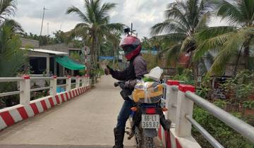 Motorcyclist on a bridge in a rural area with palm trees.