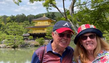 Couple posing in front of Kinkaku-ji, a gold pavilion in a garden.