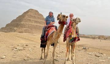 Two people riding camels near a pyramid.