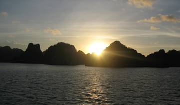 Sunset over the ocean with rocky silhouettes on the horizon.