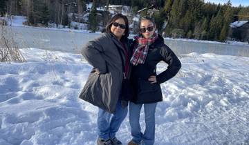 Two women posing by a snowy lake with trees in the background.