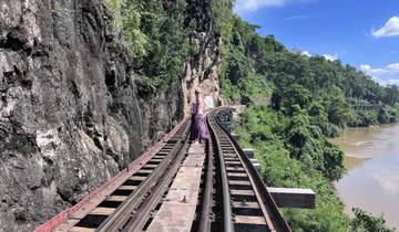 Two people walking on a historic railway track along a river and cliffs.