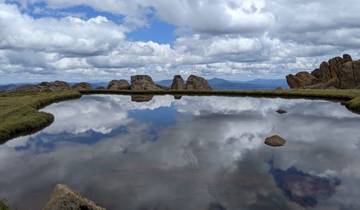 A small body of water reflecting a cloudy sky surrounded by rugged terrain.