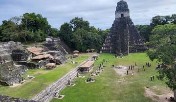 Ancient Mayan ruins with a large pyramid and people walking around.