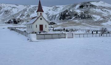 A small church and graveyard covered in snow, surrounded by hills.