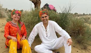Smiling couple in traditional attire sitting in a desert setting.