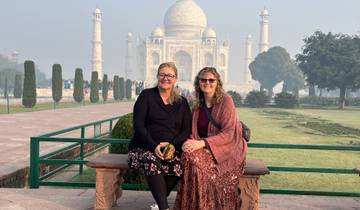 Two women sitting on a bench with the Taj Mahal in the background.