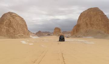 A car driving between large desert rock formations.