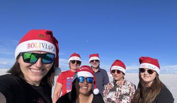 A group of people wearing Bolivia Santa hats smiling for a photo on a salt flat.