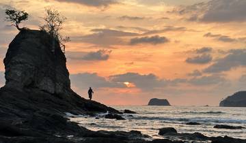Person standing on a rock during a dramatic sunset over the ocean.