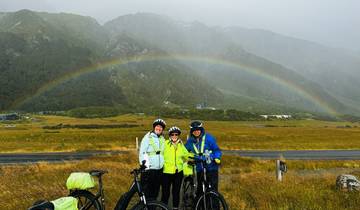 Group of cyclists with a rainbow over a mountainous landscape.