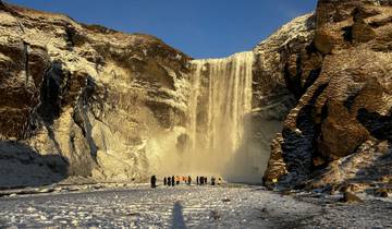 People walking toward a large waterfall in a snowy landscape.